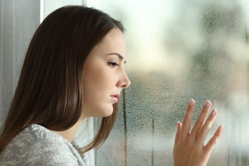 Sad woman looking rain through a window